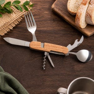 Pode incluir: Um conjunto de utensílios de campismo multi-ferramentas com cabo de madeira e componentes de aço inoxidável. A ferramenta inclui um garfo, faca, colher, saca-rolhas e abre-garrafas dobráveis, estendidos a partir do cabo central.