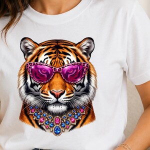 Peut inclure: Un t-shirt blanc à manches courtes avec une impression graphique représentant un tigre portant des lunettes de soleil à motif léopard rose et un collier de bijoux multicolores. Le tigre a un pelage orange, noir et blanc.