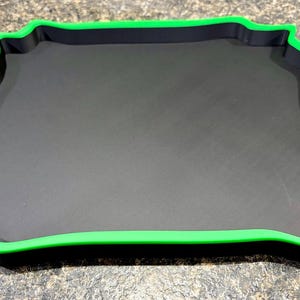 Pode incluir: Uma bandeja quadrada com uma base preta plana e uma borda elevada em verde brilhante. A bandeja apresenta um design distinto de bordas onduladas ou festonadas em todos os quatro lados, criando uma moldura decorativa ao redor da superf&iacute;cie.