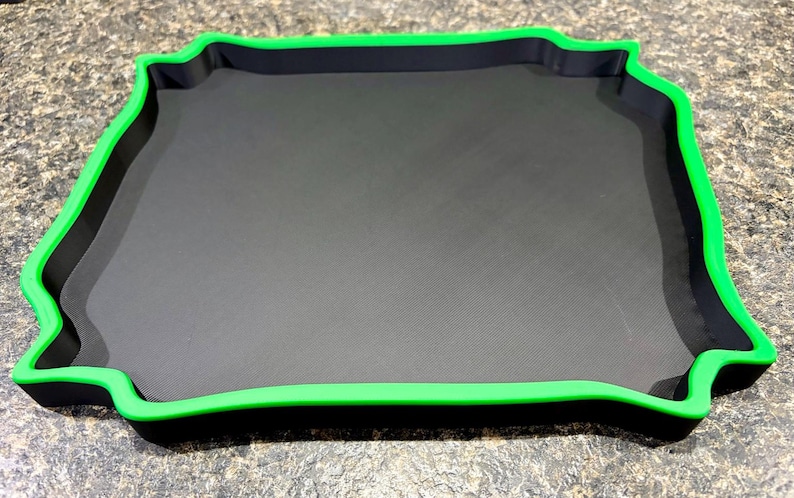 Pode incluir: Uma bandeja quadrada com uma base preta plana e uma borda elevada em verde brilhante. A bandeja apresenta um design distinto de bordas onduladas ou festonadas em todos os quatro lados, criando uma moldura decorativa ao redor da superf&iacute;cie.