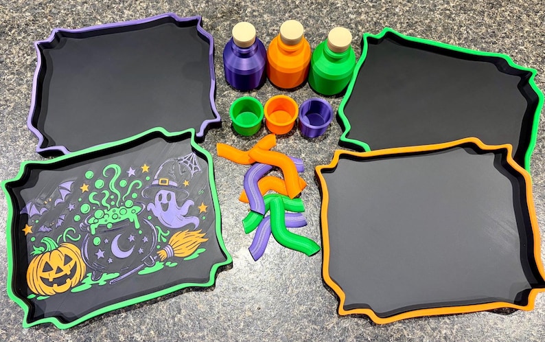 Pode incluir: Um conjunto de quatro tabuleiros retangulares com bordas recortadas em roxo, verde e laranja, tr&ecirc;s garrafas pequenas com rolhas, tr&ecirc;s copos pequenos e v&aacute;rias pe&ccedil;as de pl&aacute;stico curvas em roxo, laranja e verde, al&eacute;m de um tabuleiro com um gr&aacute;fico de Halloween.