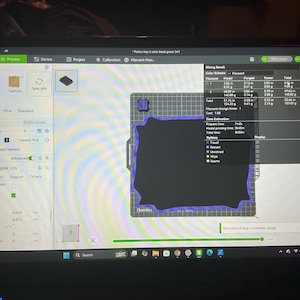 Pode incluir: Uma tela de computador exibindo a interface do software Bambu Studio para impress&atilde;o 3D. A tela mostra uma pr&eacute;via de um modelo de bandeja retangular com um centro preto e uma borda verde, junto com uma janela de resultados de fatiamento.