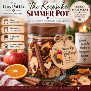 May include: A clear glass jar filled with dried apple slices, orange peels, cinnamon sticks, star anise, and cloves, topped with a dark wood lid. A round beige tag tied with twine reads Bushel Up, Buttercup and features fruit illustrations.