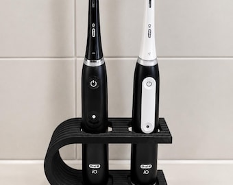 Può includere: Due spazzolini elettrici Oral-B iO, uno nero e uno bianco, sono posizionati verticalmente in un supporto in plastica nera, curvo e scanalato. Ogni spazzolino presenta un pulsante di accensione e il logo Oral-B iO sul manico.