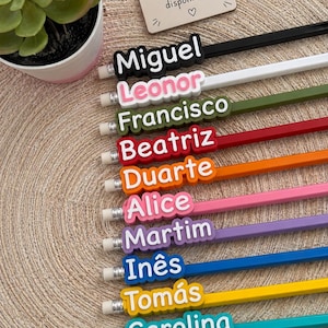 Puede incluir: Una colección de diez lápices, cada uno con un adorno de nombre en 3D personalizado en varios colores, incluyendo negro, blanco, oliva, rojo, naranja, rosa, morado, azul, amarillo y turquesa, con un letrero que dice Mais nomes disponíveis.