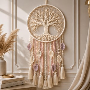 May include: A circular macrame wall hanging featuring a central tree of life design in cream cord. The piece includes hanging strands of cream and mauve crocheted leaves, cream tassels, and clear crystal beads suspended from the main hoop.