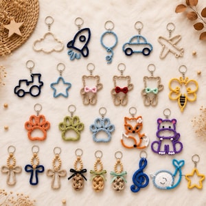 Peut inclure: Une collection de porte-clés en crochet représentant diverses formes comme une fusée, une voiture, un avion, un train, une étoile, un ours, une patte, un renard, un hippopotame, une note de musique et une baleine, avec anneau en métal.