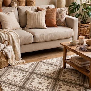 May include: A rectangular area rug featuring a repeating geometric pattern of white starburst motifs set within brown square borders. The rug is positioned on a wooden floor in front of a beige sofa adorned with various textured throw pillows.
