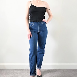 May include: A person wearing a black tank top and blue denim jeans. The jeans have a high waist and a straight leg.