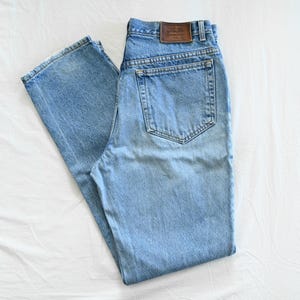 May include: Light blue denim jeans with a classic five-pocket design. The jeans have a straight leg cut and a brown leather patch on the back waistband. The denim has a faded appearance, suggesting wear and washing.