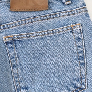 Może przedstawiać: Jasne niebieskie dżinsy z brązową sk&oacute;rzaną naszywką z napisem "Calvin Klein Jeans". Dżinsy mają tylną kieszeń z brązowym szwem.