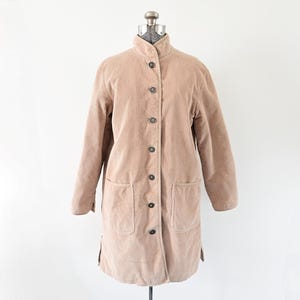 May include: A light brown corduroy coat with a mandarin collar and button-down front. The coat has two front pockets and is displayed on a mannequin. The coat is a neutral colour and has a classic design.