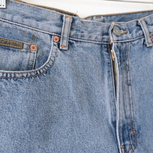 Może przedstawiać: Jasne niebieskie dżinsy z zamkiem błyskawicznym i metką Calvin Klein na przedniej kieszeni.