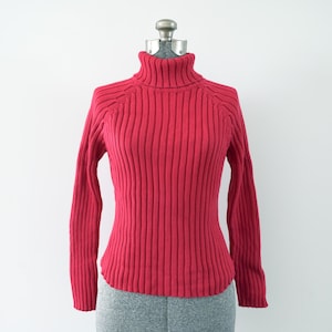Op de afbeelding: Een rode geribbelde trui met hoge hals op een mannequin.