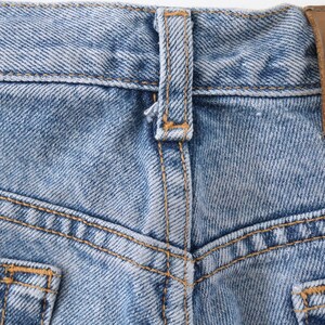 Może przedstawiać: Zbliżenie na parę jasnoniebieskich dżins&oacute;w z brązową sk&oacute;rzaną naszywką z napisem "Calvin Klein" na tylnym pasie.