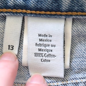 Może przedstawiać: Biała metka z czarnym tekstem, na kt&oacute;rej widnieje napis "Made in Mexico, Fabrique au Mexique, 100% Cotton- Coton". Po lewej stronie większej metki widoczna jest biała metka z czarnym tekstem, na kt&oacute;rej widnieje napis "13".