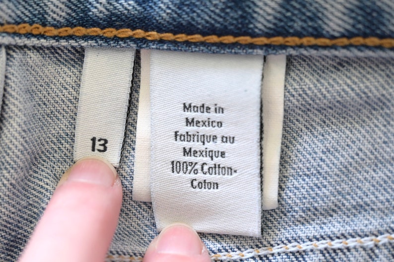 Może przedstawiać: Biała metka z czarnym tekstem, na kt&oacute;rej widnieje napis "Made in Mexico, Fabrique au Mexique, 100% Cotton- Coton". Po lewej stronie większej metki widoczna jest biała metka z czarnym tekstem, na kt&oacute;rej widnieje napis "13".