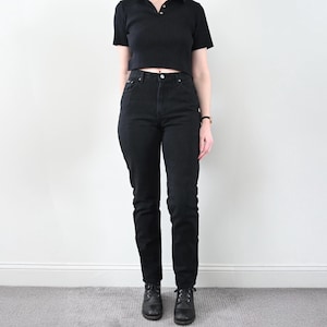 Puede incluir: Una persona lleva una camisa negra de cuello alto y pantalones vaqueros negros de cintura alta. La persona lleva botas de cuero negras.