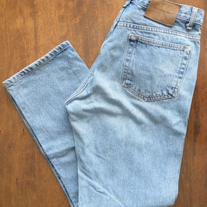 Może przedstawiać: Jasne niebieskie dżinsy z brązową sk&oacute;rzaną naszywką z napisem "Calvin Klein Jeans" na tylnej kieszeni.