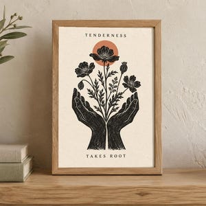 May include: A framed print featuring a black ink illustration of two hands cupping a bouquet of flowers with a terracotta circle above them. The text TENDERNESS is printed at the top and TAKES ROOT is printed at the bottom in black capital letters.