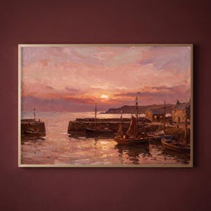 May include: An oil painting in a gold frame depicting a harbor scene at sunset. The sky is filled with pink and orange clouds above a calm sea. Several wooden sailboats are moored near stone piers, with small buildings visible on the shore.