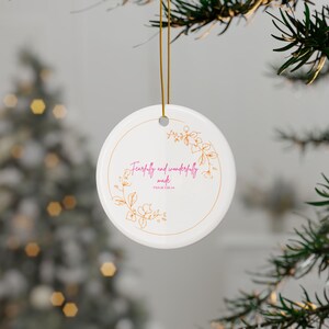 Puede incluir: Un adorno redondo de cerámica blanca que cuelga de un cordón dorado. El adorno presenta un borde circular dorado fino, una ilustración de enredadera floral dorada y el texto rosa Fearfully and wonderfully made con el texto PSALM 139:14.