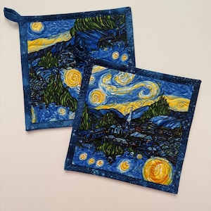 May include: Two square pot holders featuring a print of Van Gogh's "Starry Night" painting. The pot holders have a blue border with a loop for hanging. The artwork depicts a village under a swirling night sky with yellow stars and a crescent moon.