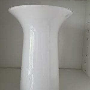 May include: A solid white vase with a smooth, glossy finish. The vase features a cylindrical body that gradually widens toward the top, creating a flared, trumpet-like opening. The design is simple and uniform, with no patterns or additional textures.