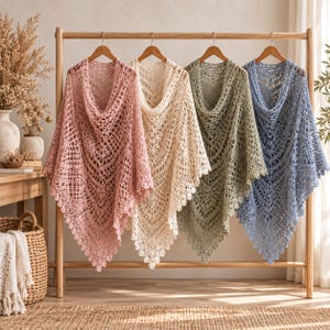 Pode incluir: Quatro xales triangulares de crochê pendurados em um suporte de madeira. Os xales são nas cores rosa seco, creme, verde sálvia e azul acinzentado. Cada peça apresenta um padrão de renda intrincado com bainha pontiaguda e borda festonada.