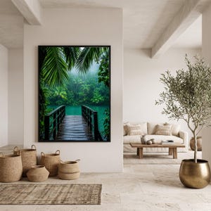 May include: A framed wall art print depicting a wooden pier extending into a calm, turquoise lake surrounded by a lush, misty tropical rainforest. The scene features vibrant green palm fronds framing the top and sides of the landscape view.