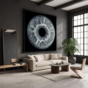 Op de afbeelding: Een groot vierkant kunstwerk aan de muur met een contrastrijke, gedetailleerde zwart-wit macrofoto van een menselijke iris, met complexe, vertakte witte filamenten die uitstralen vanuit een zwarte pupil, in een dunne zwarte lijst.