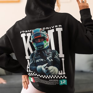 May include: A black hooded sweatshirt featuring a large graphic on the back of a Formula 1 driver wearing a helmet. The text reads FORMULA DRIVER, KIMI ANTONELLI, SILVER ARROWS, and the number 12. The design includes a checkered pattern and an Italian flag.