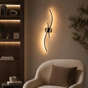 Peut inclure: Une applique murale noire composée de deux bras métalliques fins et incurvés s'étendant verticalement depuis une plaque de montage carrée centrale, diffusant une lueur chaude et douce contre le mur pour un éclairage d'ambiance.