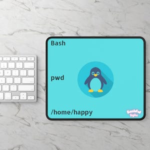 May include: A rectangular light blue mouse pad with a black border featuring a dark blue penguin graphic inside a circle. The text reads Bash, pwd, /home/happy, and Bashful Byte in the bottom right corner, printed in black and white.