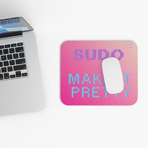 May include: A rectangular mouse pad with a pink to light pink gradient background. The text SUDO MAKE IT PRETTY is printed in a blue pixelated font. A white computer mouse rests on the pad, and a silver laptop is positioned to the left.