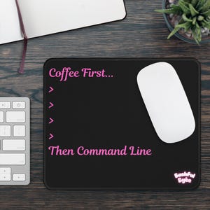 May include: A rectangular black mouse pad featuring pink text that reads Coffee First... followed by four pink greater-than symbols and the text Then Command Line. In the bottom right corner, there is a small pink logo that reads Bashful Byte.