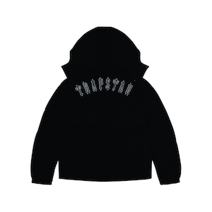 Könnte beinhalten: Eine schwarze Kapuzenjacke mit dem Wort TRAPSTAR, das in einer weißen Schrift im gotischen Stil auf den oberen Rücken gestickt ist. Das Kleidungsstück hat lange Ärmel mit elastischen Bündchen und eine große Kapuze vor weißem Hintergrund.