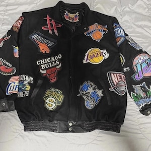 Può includere: Una giacca varsity nera caratterizzata da numerose toppe ricamate con i loghi di varie squadre di basket professionistiche, tra cui Chicago Bulls, Los Angeles Lakers e Seattle Sonics, con polsini in pelle e chiusura frontale con bottoni a pressione.