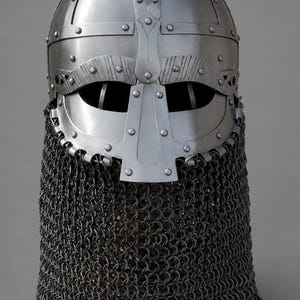 May include: A silver-coloured metal helmet featuring a rounded dome, a central vertical nose guard, and horizontal eye openings. The helmet is constructed with riveted metal plates and includes a dark grey chainmail aventail attached to the base.