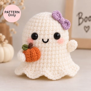 May include: A cream-coloured crocheted ghost figurine featuring a small orange pumpkin with a green stem, a purple bow on its head, black bead eyes, a stitched smile, and pink blush marks. A circular pink label with the text PATTERN Only is visible.