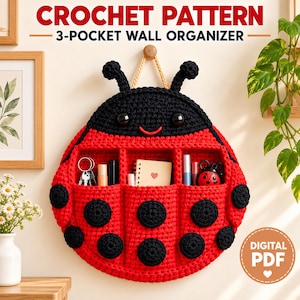 May include: A crochet pattern for a 3-pocket wall organizer shaped like a ladybug. The red and black ladybug features two antennae, large eyes, and a smiling mouth. The three pockets contain various small items like keys and pens. Text reads CROCHET PATTERN 3-POCKET WALL ORGANIZER and DIGITAL PDF.