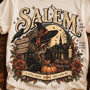 May include: A cream-colored t-shirt featuring a graphic of a witch in a hat, a black cat, a pumpkin, and a castle. Text includes SALEM, EST. 1692, POTIONS, SPELLS, APOTHECARY, WITCHES HISTORY MYSTERY, and A LITTLE MAGIC GOES A LONG WAY.