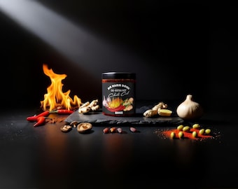 May include: A glass jar of No Harm Done OG Extra Hot Chili Oil with a black lid, centered on a dark stone slab. The label features text and a flame graphic. Surrounding the jar are fresh red chili peppers, ginger root, garlic, and mushrooms.