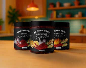 May include: Three glass jars of No Harm Done chili oil with black labels. The center jar is labeled Yuzu Shiitake, featuring illustrations of yuzu, garlic, and red chili peppers. The jars contain 6 oz of product each, with black lids.