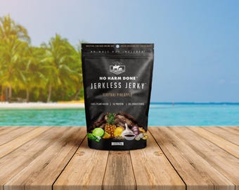 May include: A black stand-up pouch of No Harm Done Jerkless Jerky in Teriyaki Pineapple flavor. The label features text including 100% plant-based, 5g protein, 0% cholesterol, and animals not included, with images of pineapple, lime, and garlic.