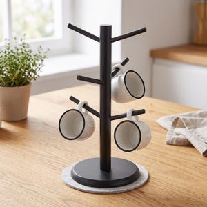 May include: A black mug tree stand with a central vertical pole and six angled branches for hanging mugs. The stand features a round base resting on a circular grey felt pad. Three white ceramic mugs with black rims are hanging on the branches.