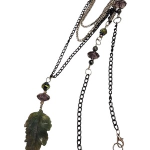May include: A layered necklace with a green leaf pendant and black and silver chains. The necklace features iridescent purple and green beads.