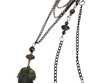 May include: A layered necklace with a green leaf pendant and black and silver chains. The necklace features iridescent purple and green beads.