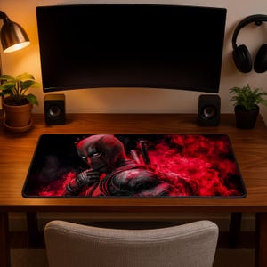 Könnte beinhalten: Eine rechteckige Schreibtischunterlage mit einer grafischen Illustration der Figur Deadpool in einem schwarzen Anzug mit roten Akzenten vor einem leuchtend roten, rauchigen Hintergrund. Die Figur ist bis zur Brust abgebildet.