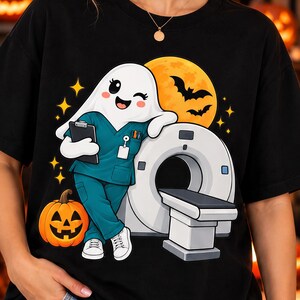 May include: A black t-shirt featuring a graphic of a winking ghost dressed in teal medical scrubs, holding a clipboard, and leaning against a white CT scanner. The design includes a bright orange jack-o'-lantern, a full moon, and black bats.